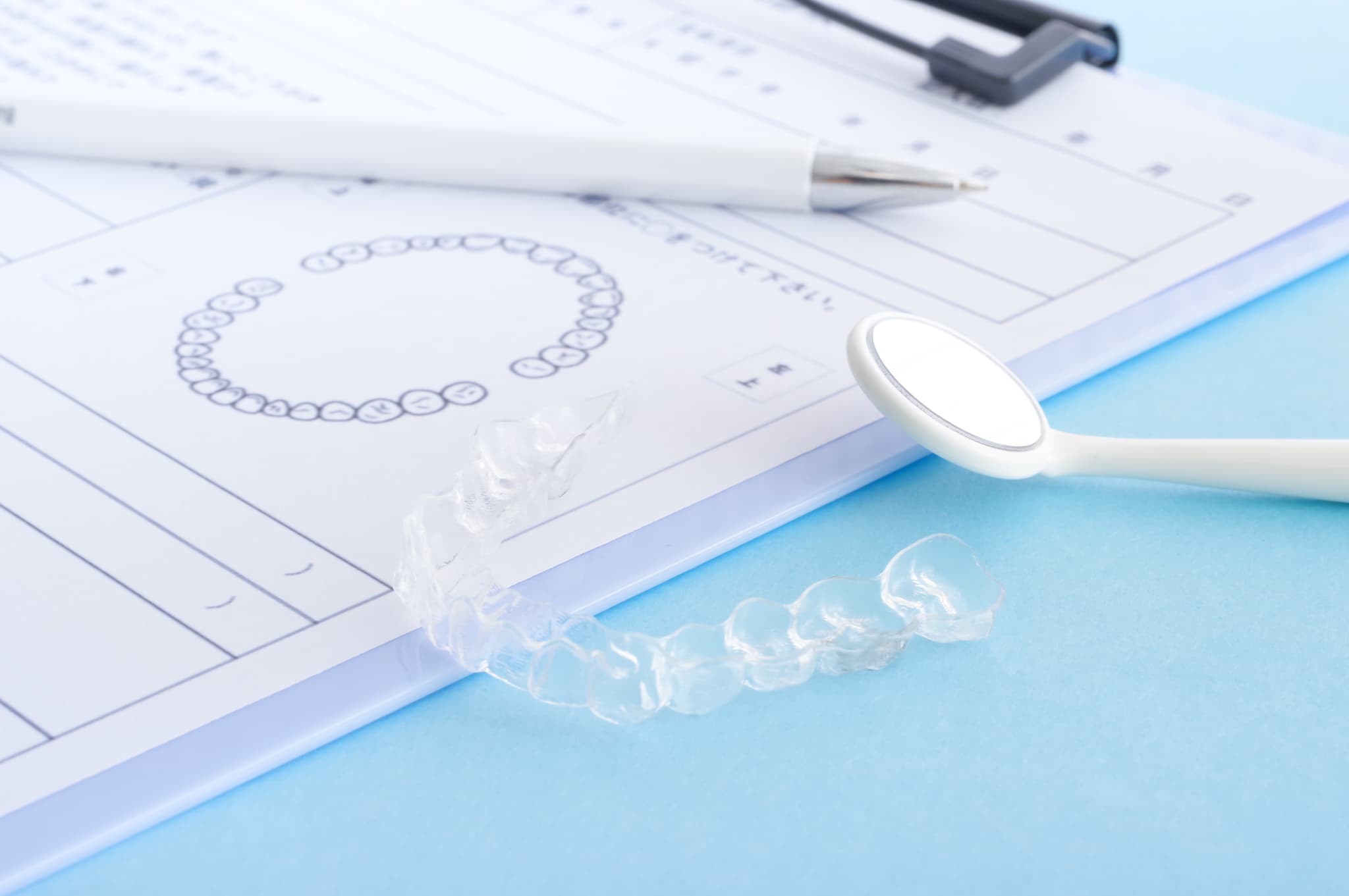 インビザラインの治療を長引かせないために定期的にチェックや調整を受けることを示すカルテとミラーとマウスピース